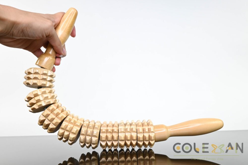 Wood Roller Massager A person holding a wooden massage roller on a table. The roller is long and cylindrical, with spikes like a corn. It is made of light colored wood.