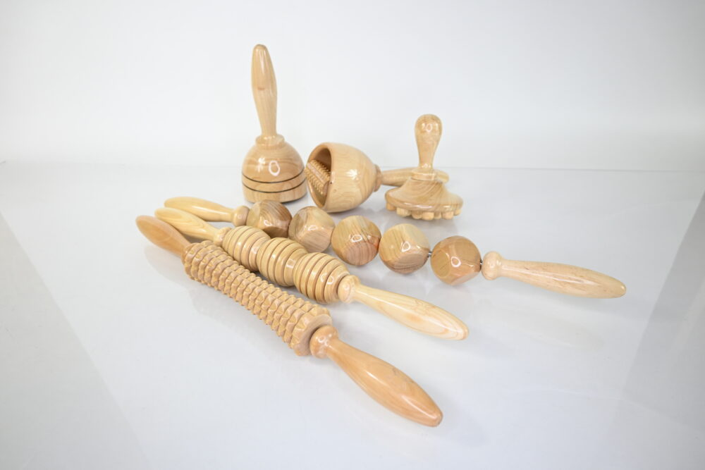 Wooden therapy massage set with 7 pine wood massagers in a clear light color, coated for durability. Includes 2 cups (one with a roller), 3 engraved body rollers (one with 5 cubes), a body gua sha, and a mushroom tool with fingers, perfect for full body sculpting.