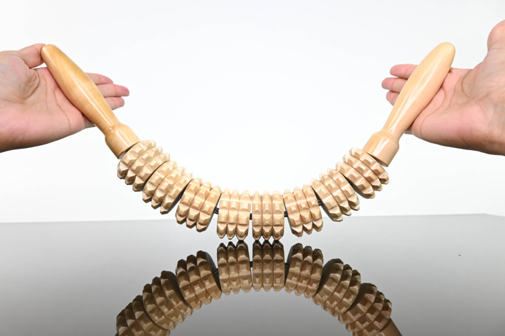 Mano sosteniendo un rodillo mazorca de maderoterapia flexible en madera color natural, ideal como masajeador de madera para celulitis, esculpir cintura y reducir grasa.