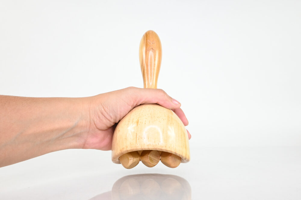 Hand holding wooden dice cup roller for targeted massage
